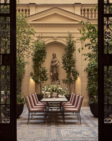 Sir Prague Courtyard communal table pink chairs stone statue trees plants mosaic floor