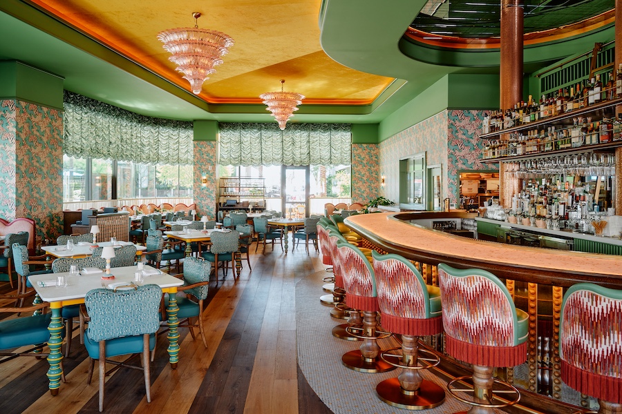 Bar Issi the Thompson Hotel maximalist 1970s mediterranean italian coastal glamor dancing tiger wallcovering wallpaper pink bar stools patterned chairs indoor plants green molding doors pink feather chandelier mohair fringe bar stools
