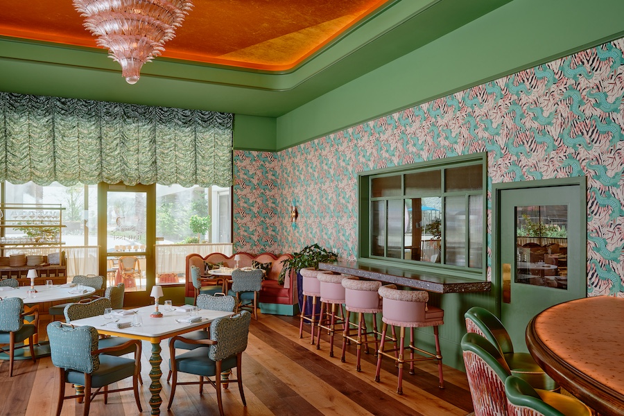 Bar Issi the Thompson Hotel maximalist 1970s mediterranean italian coastal glamor dancing tiger wallcovering wallpaper pink bar stools patterned chairs indoor plants green molding doors pink feather chandelier