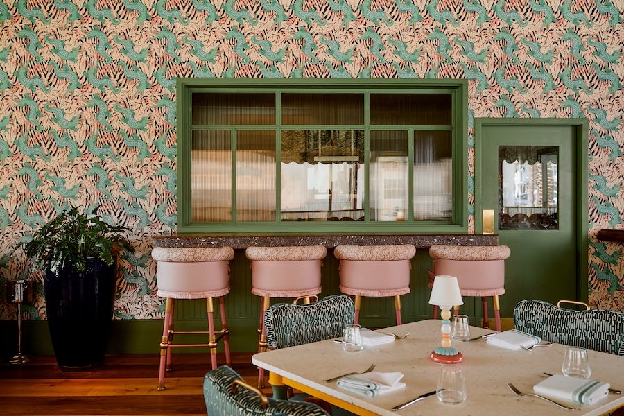 Bar Issi the Thompson Hotel maximalist 1970s mediterranean italian coastal glamor dancing tiger wallcovering wallpaper pink bar stools patterned chairs indoor plants green molding doors