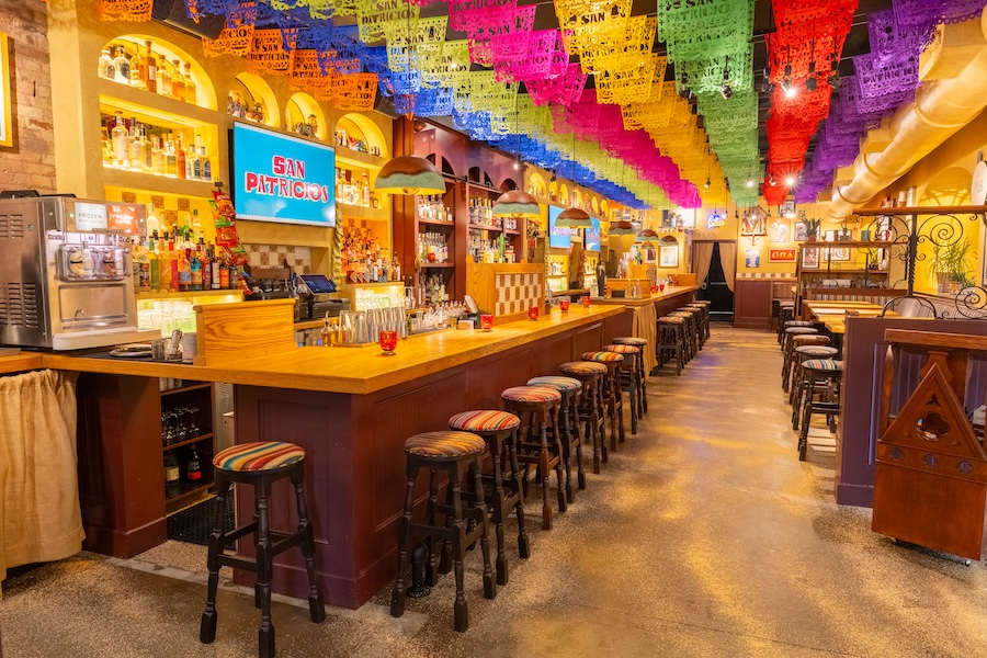 San Patricios jersey city pub cantina mexican irish design yellow walls curtains patterned tables wall art prints papel picado colorful rainbow tissue paper bar counter arched liquor shelves